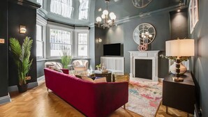 Un salon avec un canapé rouge, une cheminée, un téléviseur et un lustre.
