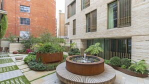Un cortile con una fontana circolare circondata da fioriere e un insieme di edifici in mattoni e pietra.