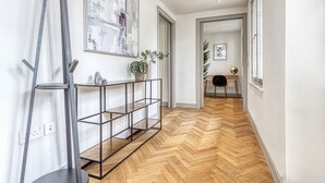 Un corridoio con pavimento a spina di pesce, un tavolo consolle in metallo, una pianta in vaso e un quadro appeso al muro.