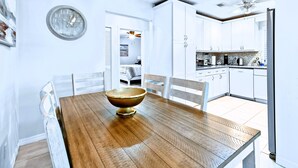 Un comedor con una mesa y sillas de madera, un reloj de pared y una cocina al fondo.