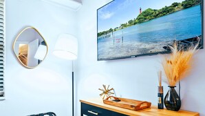 Una habitación moderna con una consola de madera, un escritorio negro, un espejo, una lámpara y un cuadro de una playa.