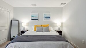 Ein Schlafzimmer mit einem Bett, zwei Nachttischlampen, einem Spiegel und zwei an der Wand befestigten Bildern.