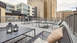 Eine Dachterrasse mit Außenbestuhlung und Blick auf umliegende Gebäude, bewölkter Himmel.