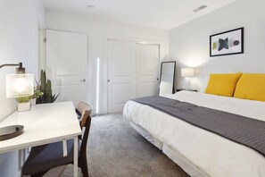 A bedroom with a bed, a desk, a chair, a lamp, and a door. - 2BR Executive Downtown Retreat (Detroit)