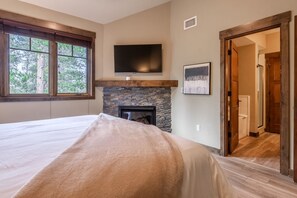 A bedroom with a large bed, a stone fireplace, a television, and a door leading to another room. - Woodwinds 32 | 2 Private Decks | Hot Tub (Mammoth Lakes)