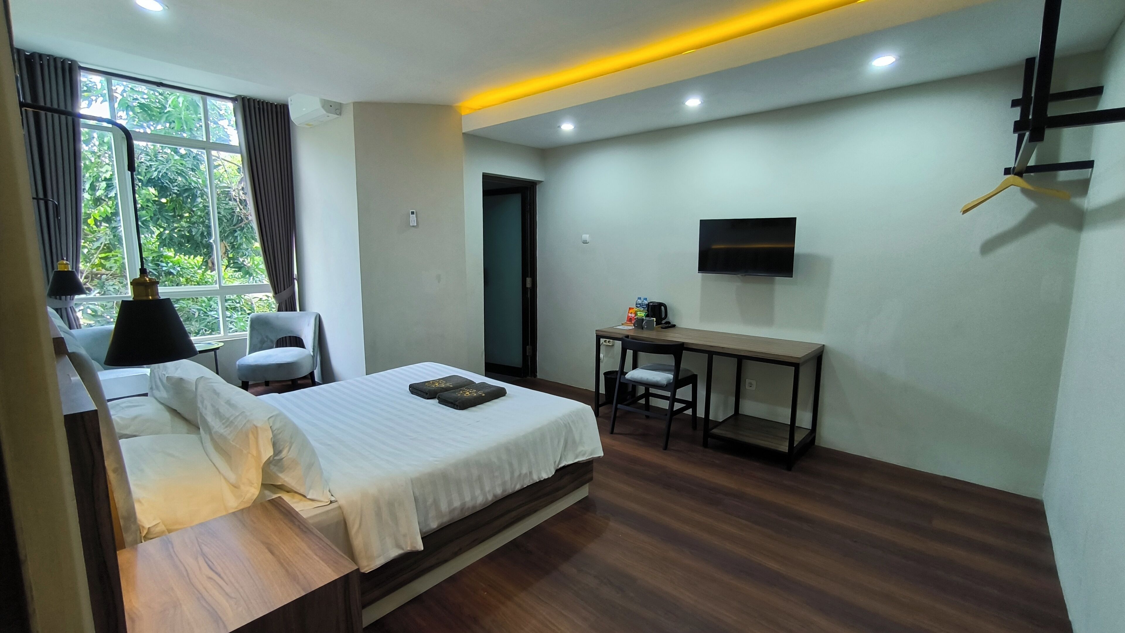 A hotel room with a bed, a desk, a chair, a TV, and a window with curtains.