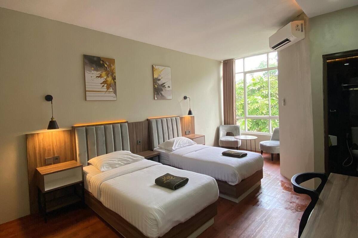 A hotel room with two beds, a desk, a chair, and a window with curtains.