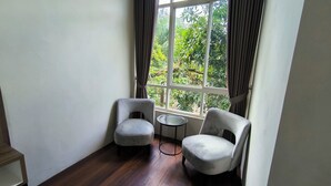 Habitación de esquina con dos sillones grises, una mesita redonda y una ventana con cortinas.