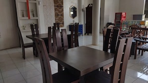 Un comedor con mesas y sillas de madera, piso de baldosas y una pared decorada con paneles y un espejo.