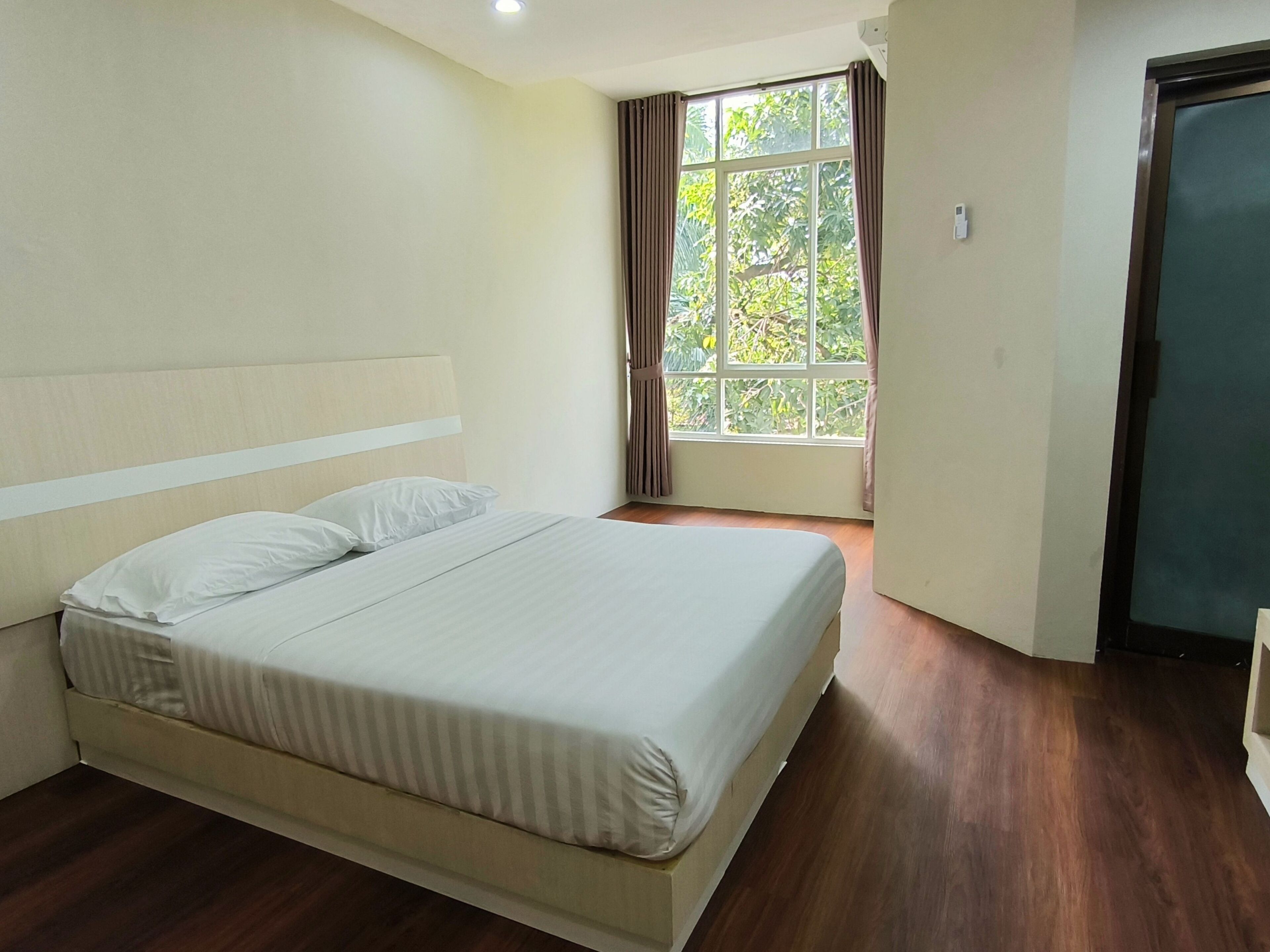 Une chambre propre et bien éclairée, avec un grand lit, une fenêtre avec des rideaux et une porte.