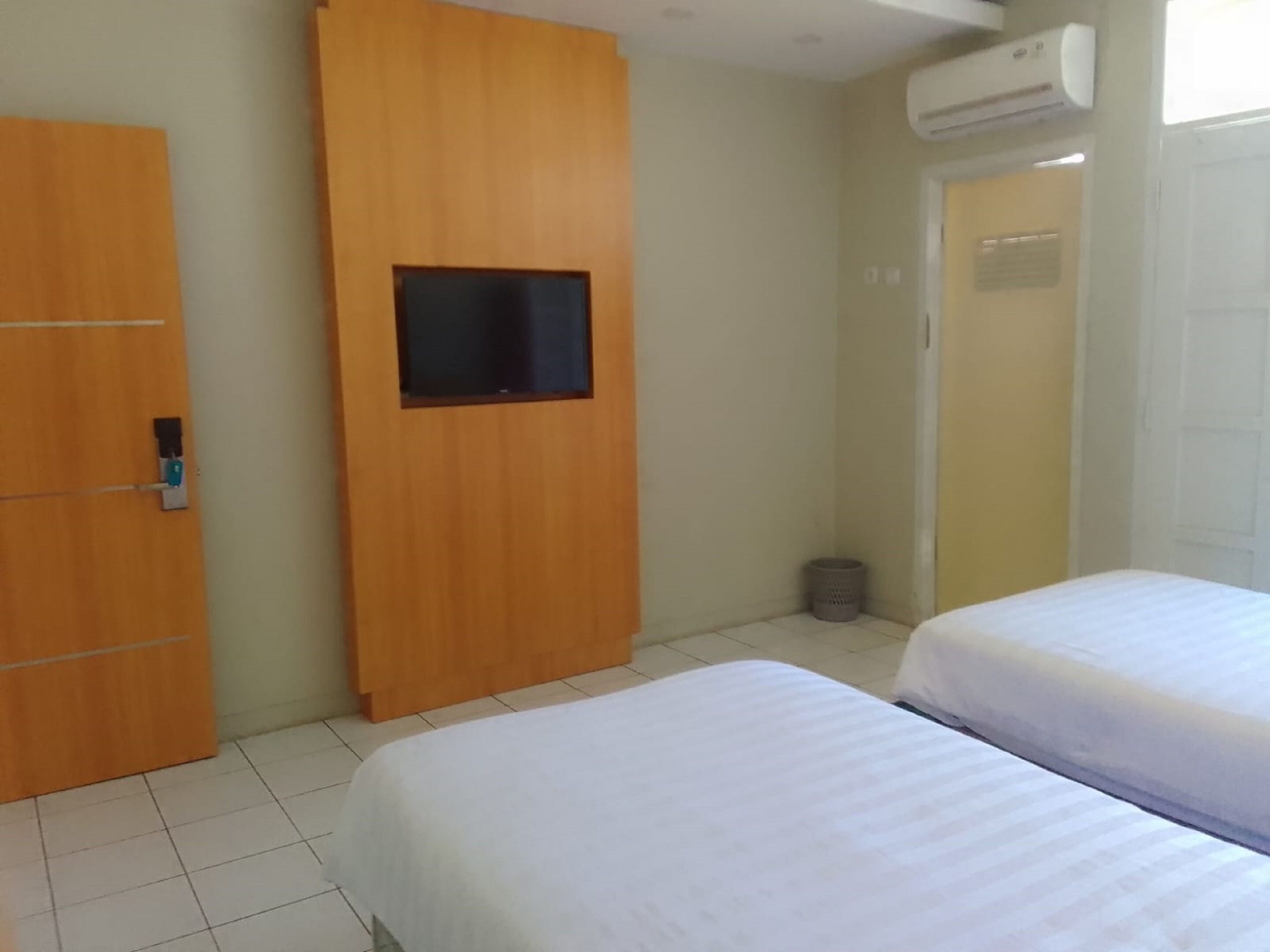 Ein Zimmer mit zwei Betten, einem Holzschrank, einem an der Wand montierten Fernseher und einer Klimaanlage.