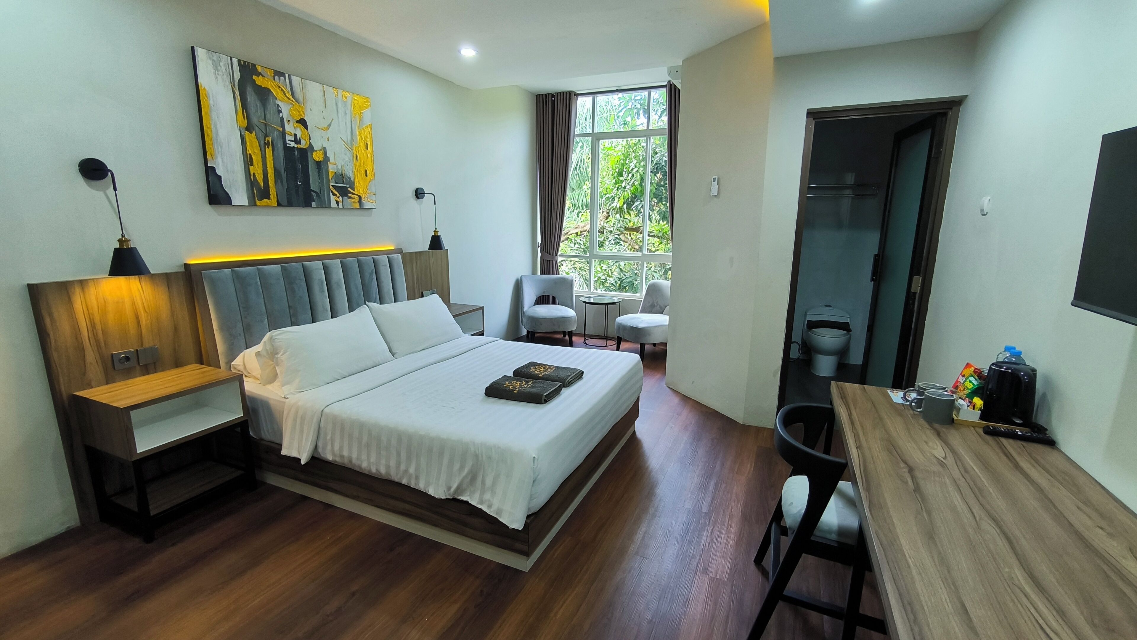 A modern hotel room with a large bed, a desk, and a seating area with two chairs.