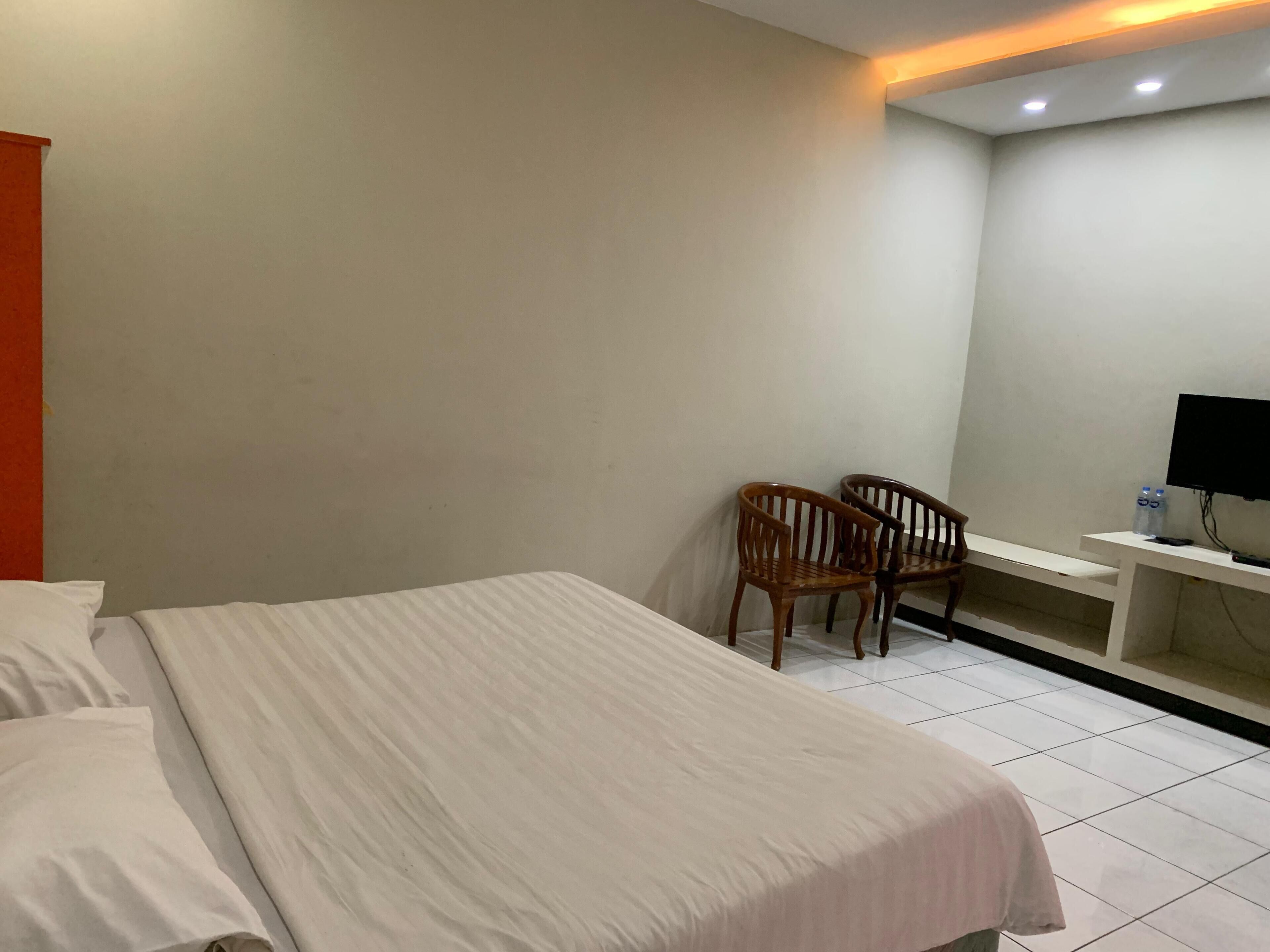 A hotel room with a bed, two wooden chairs, a TV, and a small table.