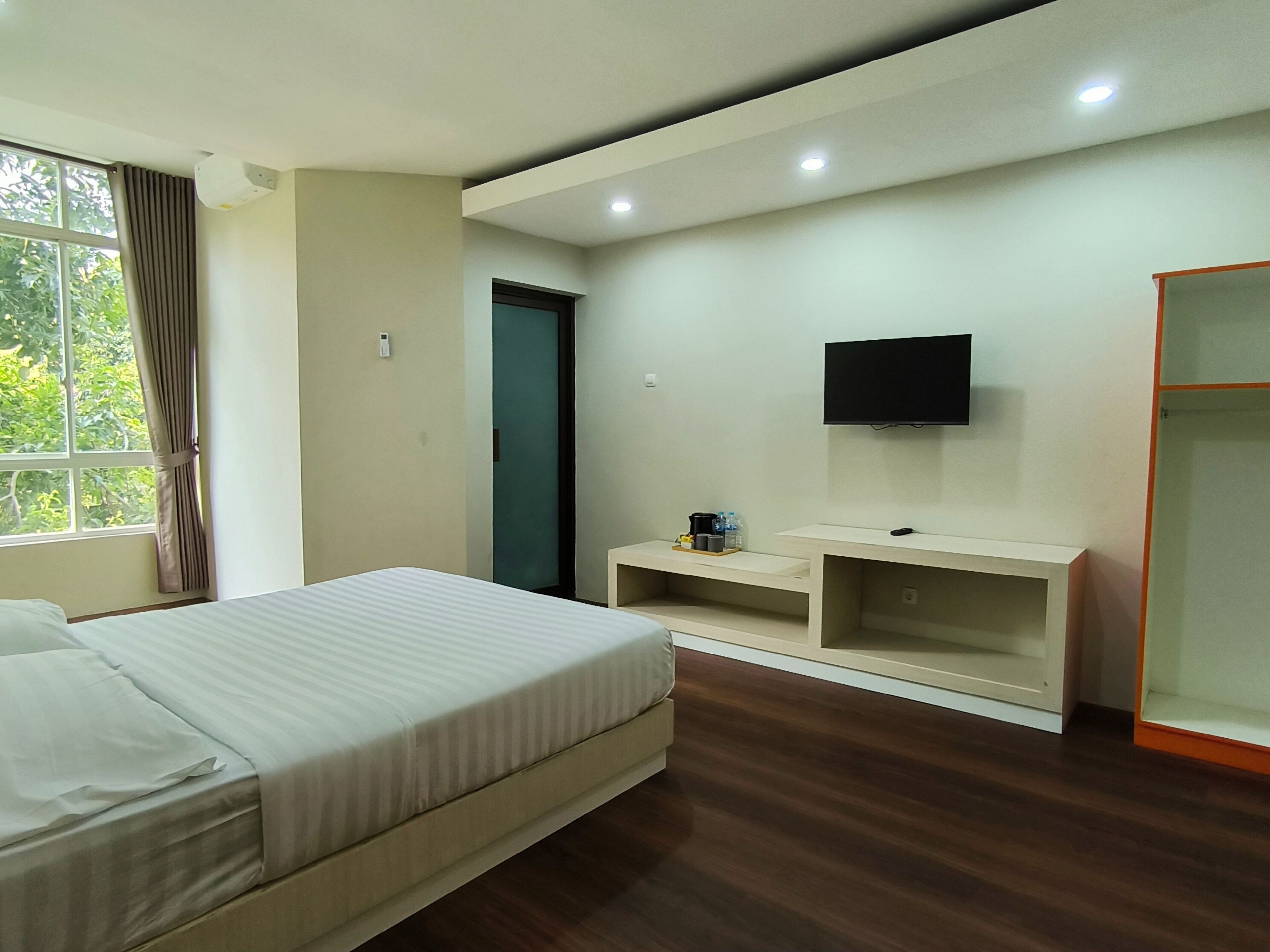 Una habitación de hotel con cama, televisión, armario, escritorio y ventana con cortinas.