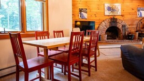 A wooden interior with a fireplace, a dining table with chairs, and artwork on the walls. - Charming Okemo Home: Hot Tub, Fireplace, Sleeps 9 (Ludlow)