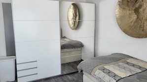 Een slaapkamer met een grote kledingkast, een bed met beddengoed met een patroon, en een decoratief wandobject.