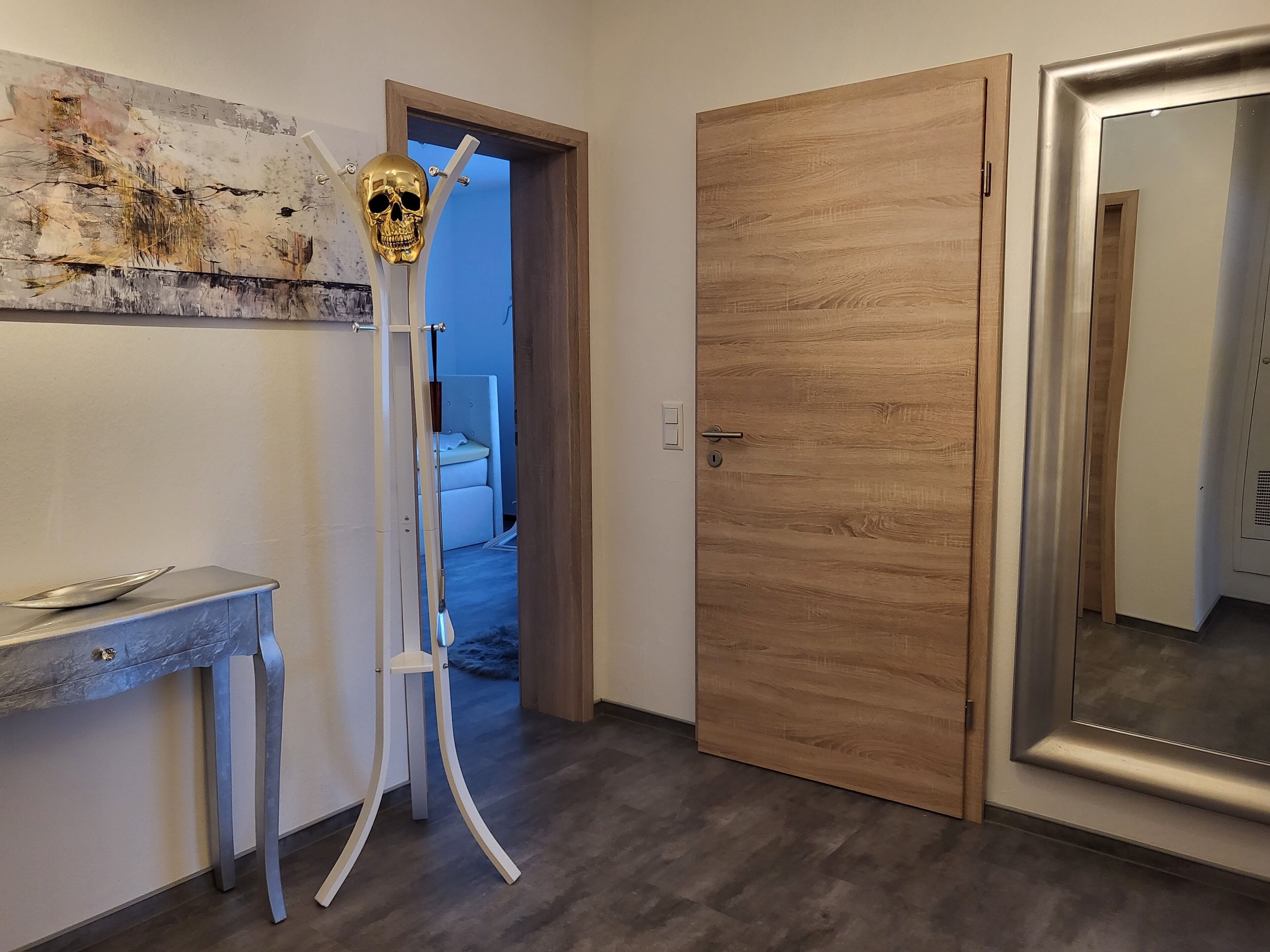 Ein Flur mit einer Holztür, einer weißen Wand mit einer strukturierten Malerei und einer Metallskulptur.