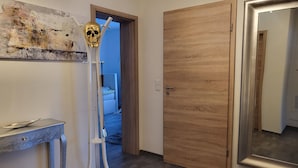 Een gang met een houten deur, een witte wand met een reliëfschildering en een metalen sculptuur.