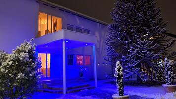Ein modernes Gebäude mit überdachtem Außenbereich, schneebedeckter Bepflanzung und einem großen Baum.