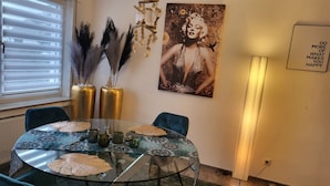 Een eethoek met een glazen tafel, stoelen, decoratieve vazen en een aan de muur hangend schilderij.