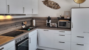 Een moderne keuken met witte kastjes, een houten aanrecht, een ingebouwde oven, een magnetron en een koffieapparaat.