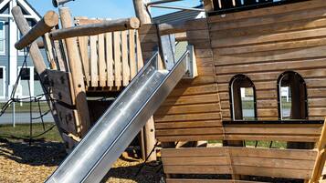 A wooden play structure with a slide, climbing elements, and windows.