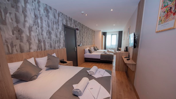 A hotel room with two beds, a desk, a TV, and a large window. - Mahya Hotel (Istanbul)