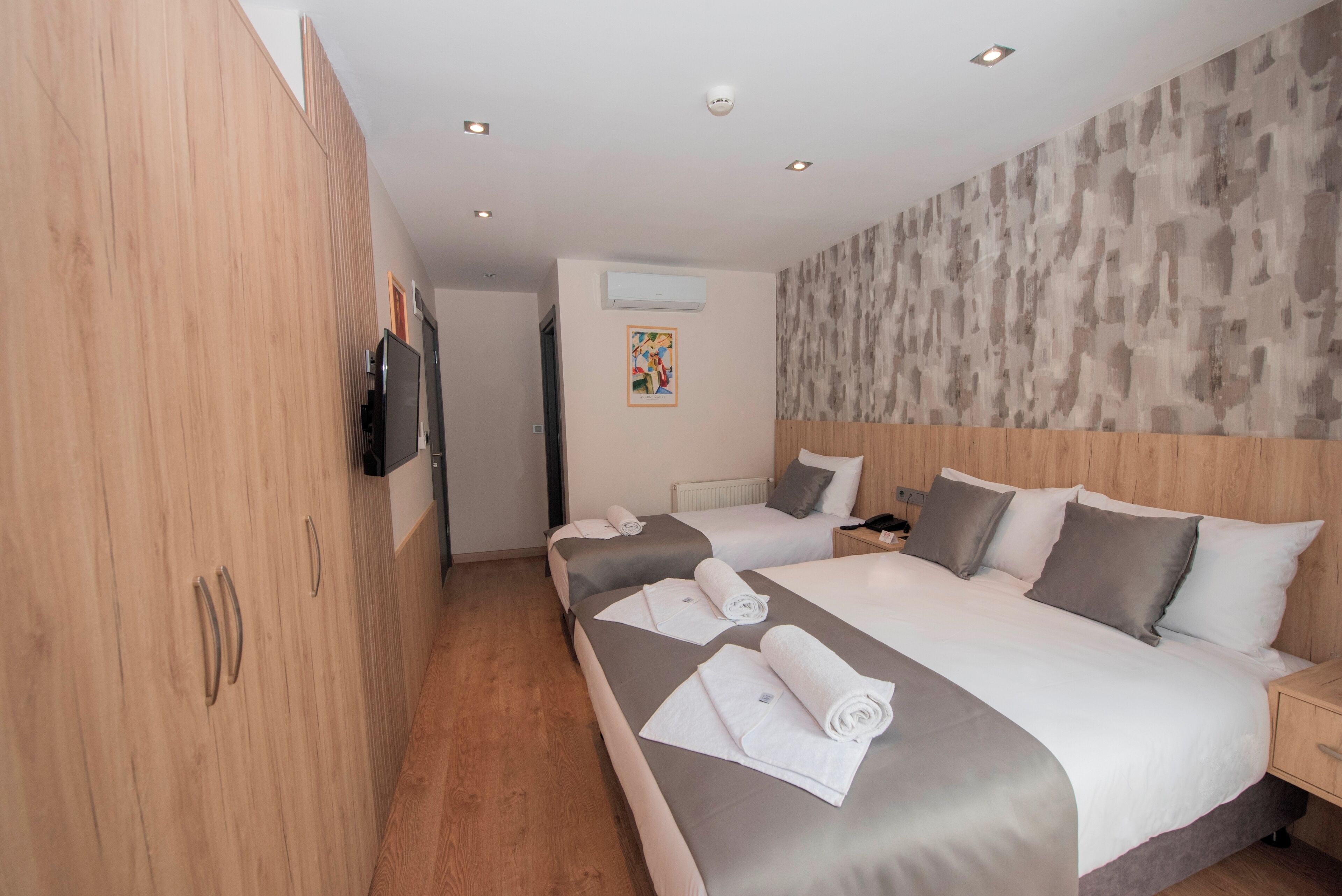 Une chambre d’hôtel avec deux lits, une armoire en bois et un téléviseur fixé au mur.