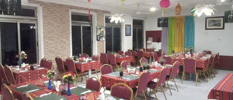 Une salle de banquet avec de nombreuses tables dressées pour le repas, des chaises et des ventilateurs de plafond.