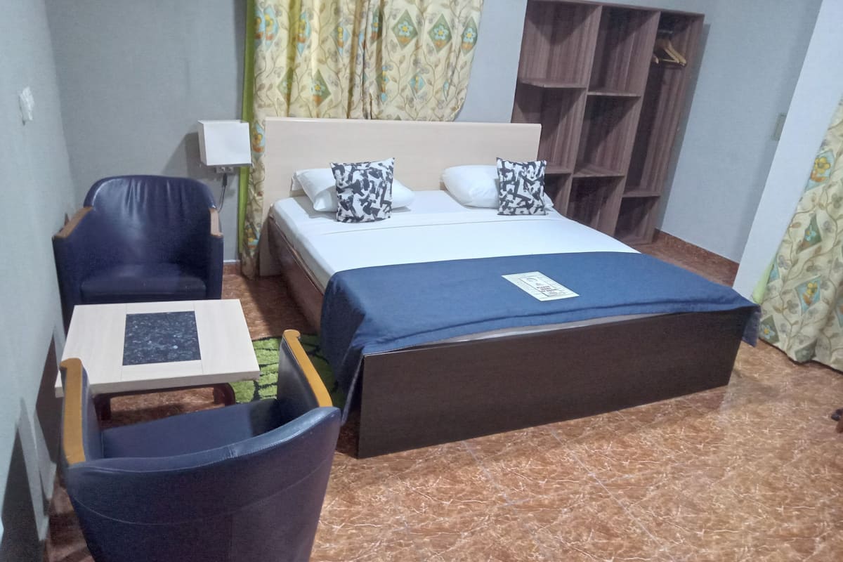 Habitación de hotel con cama, escritorio, silla, armario y cortina.