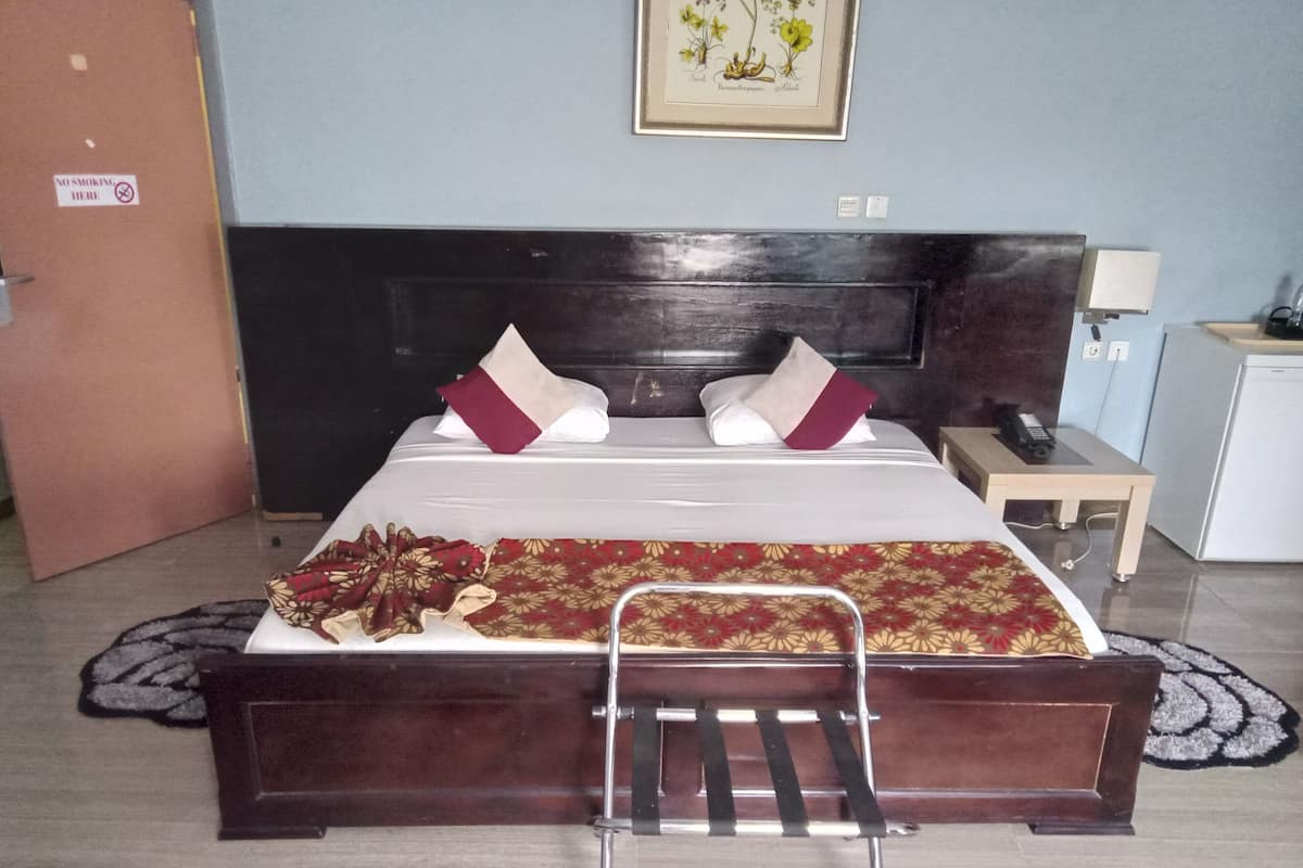 Una cama bien hecha con cabecera de madera, una mesita de noche con lámpara y un escritorio pequeño con teléfono.