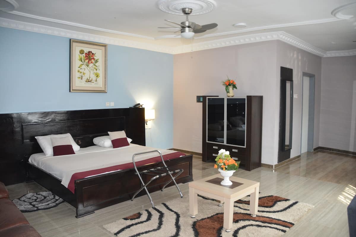 Habitación de hotel con cama, escritorio, armario, ventilador de techo y una obra de arte floral enmarcada en la pared.