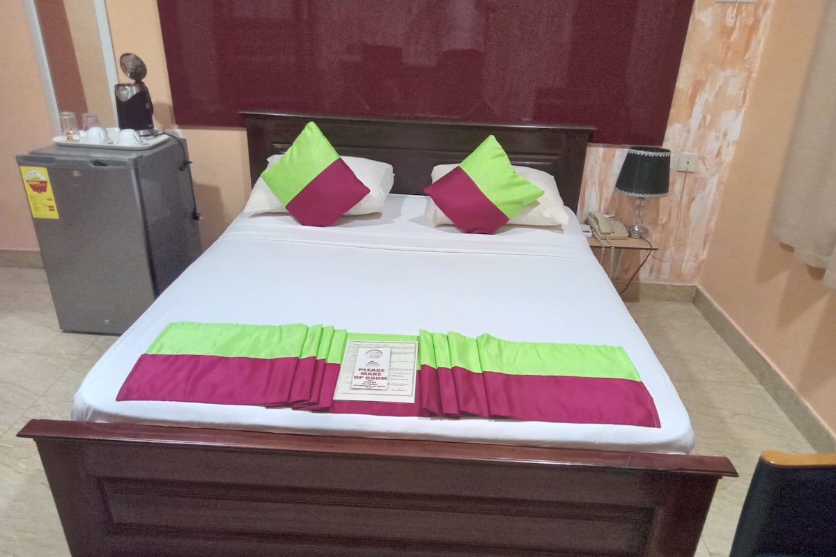 Una cama bien tendida con colcha verde y rosa, almohadas y una señal sobre la cama.