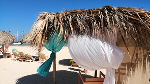 Eine Strandhütte mit einem Reetdach, umgeben von Liegestühlen und einem kleinen Tisch.