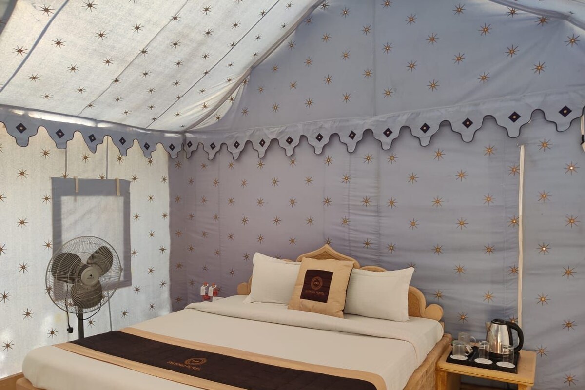 Ein Zelttyp-Zimmer mit einem Bett, einem Nachttisch mit Wasserkocher und einem Ventilator.