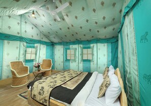 A room with a bed, two wicker chairs, a small table with a vase, and a ceiling fan.