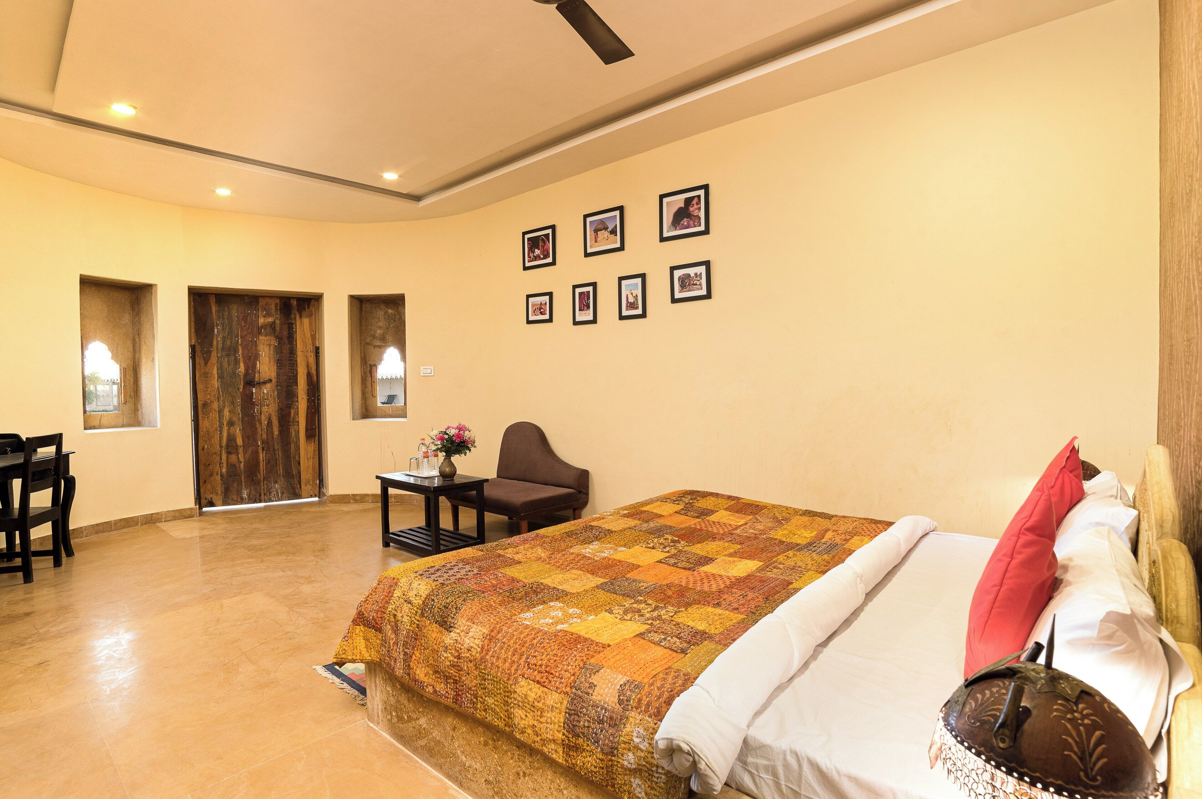 A hotel room with a large bed, a desk, and a chair. There are pictures on the wall and a wooden door.
