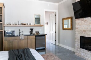 A compact kitchen with a microwave, coffee maker, and dishwasher, a bed with a blanket, a fireplace, and a TV mounted on the wall.