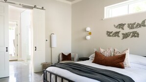 A bedroom with a bed, bedside table, lamp, and decorative wall art. - Cozy Modern Suite with Hot Tub (Fredericksburg)