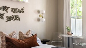 A bedroom with a bed, a ceiling fan, a window, a small table, and a chair. - Cozy Modern Suite with Hot Tub (Fredericksburg)