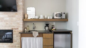 A kitchen with a brick wall, a flat-screen TV, a microwave, a coffee maker, and a dishwasher. - Cozy Modern Suite with Hot Tub (Fredericksburg)