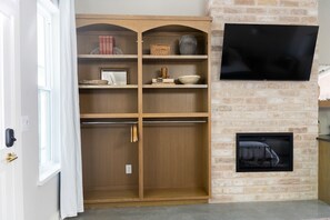 A room with a wooden shelving unit, a flat-screen TV, and a fireplace.