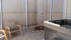 A wooden deck with a hot tub, a chair, and a shower area. - Cozy Modern Suite with Hot Tub (Fredericksburg)