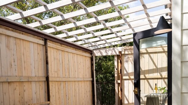 A wooden deck with chairs, a pergola, and a glass door leading to an outdoor dining area. - Cozy Suite with Hot Tub in Fredericksburg (Fredericksburg)