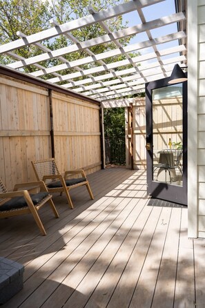 Une terrasse en bois avec des chaises, une pergola et une porte vitrée donnant sur un espace de repas extérieur.