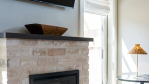A modern living room with a fireplace, a flat-screen TV mounted above it, and a glass table with a lamp. - Cozy Suite with Hot Tub in Fredericksburg (Fredericksburg)