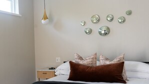 A neatly made bed with a brown pillow, a bedside table with a lamp, and decorative glass spheres on the wall. - Cozy Suite with Hot Tub in Fredericksburg (Fredericksburg)