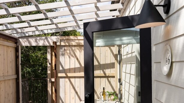 Une terrasse en bois avec une porte vitrée donnant sur une pièce où se trouvent une table et des chaises.