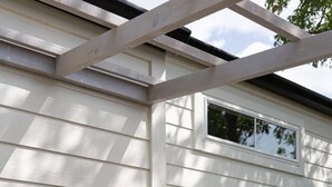 Un bâtiment dont l’extérieur est recouvert de panneaux blancs, avec une porte noire dotée de panneaux de verre et des appliques murales noires.