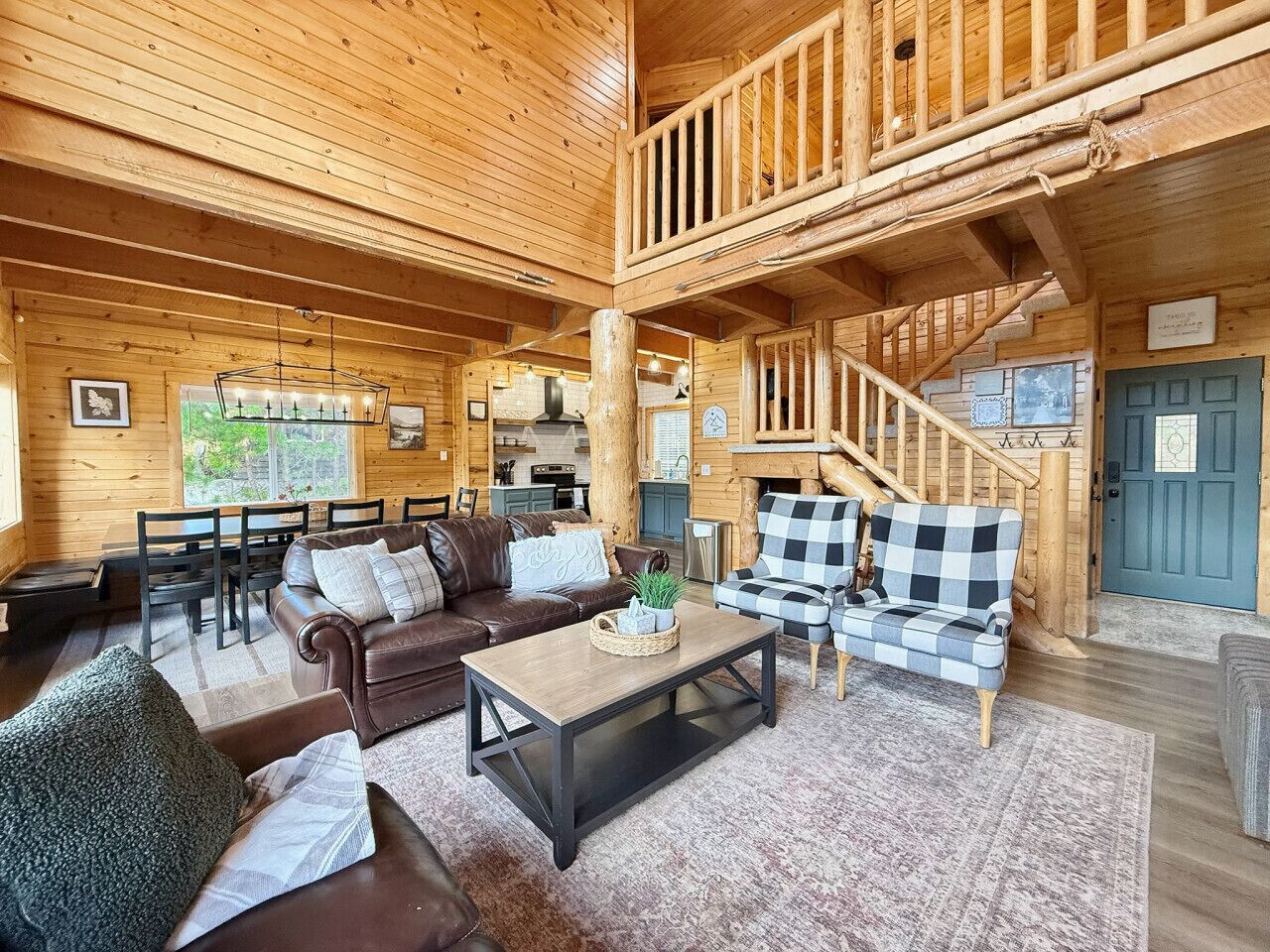 L’intérieur d’une cabane en rondins comprend un coin repas, un salon avec un canapé et des fauteuils, un escalier et une porte bleue.